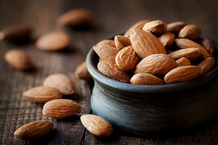 Almonds in a black bowl against dark rustic wooden background