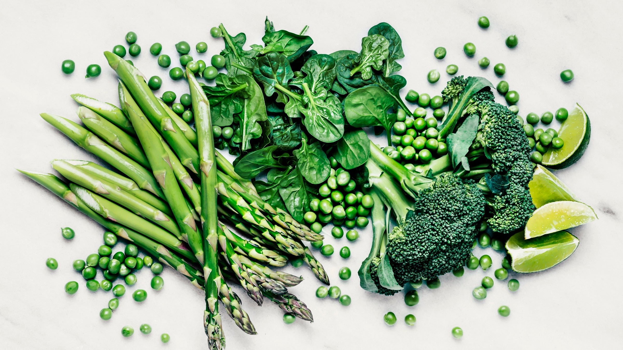 Green vegetables and lime slices splayed out on white background